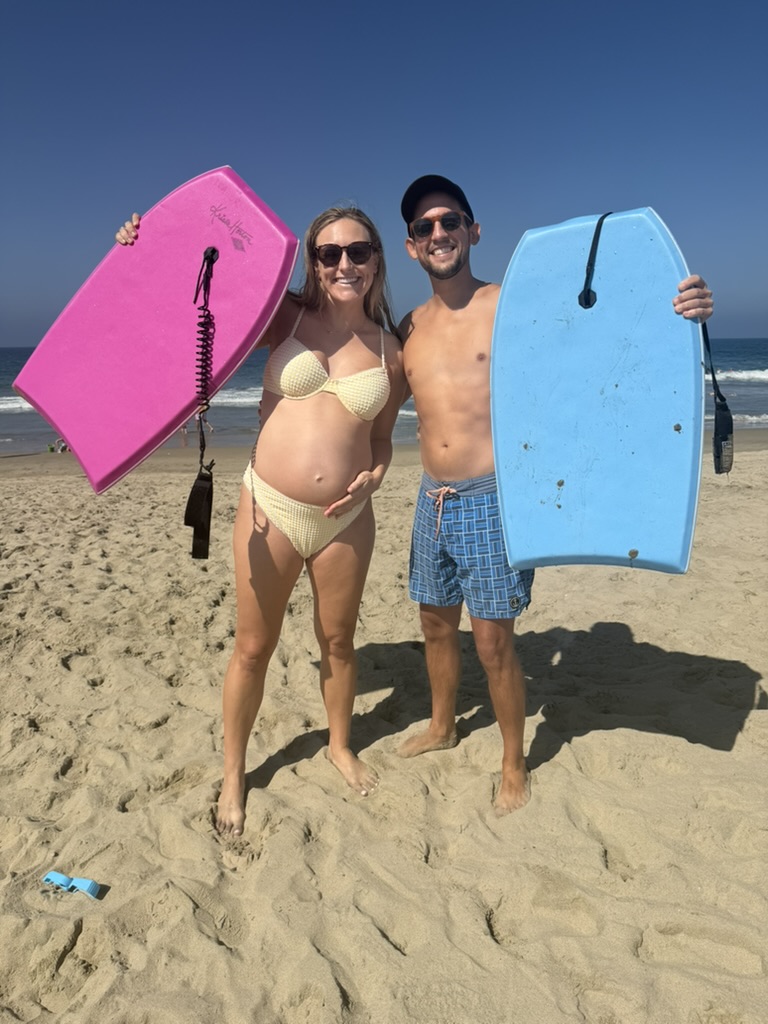 Aubrey and Sammie on the beach holding a pink and a blue boogie board
